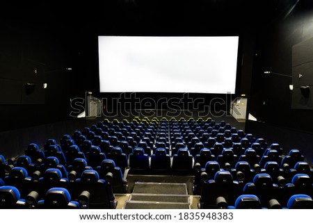 Cinema theater interior with screen and blue seats.Wide shot view from the back of an empty auditorium with lights on stock photo