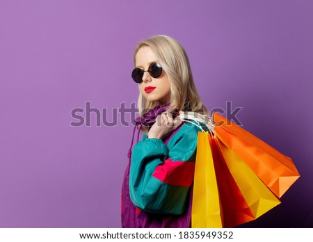 Style woman in 80s windbreaker and roud sunglasses hold shopping bags on purple background