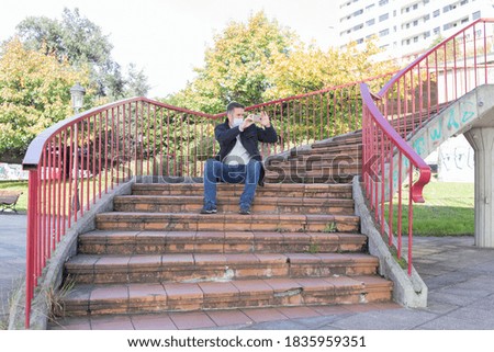 Man sitting on the stairs taking a photo with the mobile on a sunny day