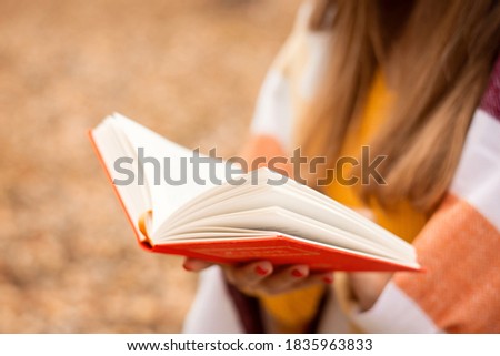 Close-up picture of a book in hands of a girl. Girl reading a book in fall park