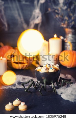 Candies and cookies in shape of an eye for holiday of halloween, dark background with cobwebs, pumpkins and candles.