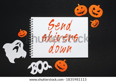 Happy halloween holiday concept. Notepad with text Send shivers down on black background with bats, pumpkins and ghosts