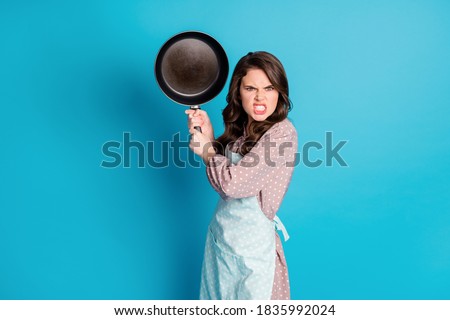 Photo of crazy angry mad outraged lady hold hands kitchen utensil frying, pan cooking dinner fight boyfriend beating him wear apron dotted dress isolated blue color background Royalty-Free Stock Photo #1835992024