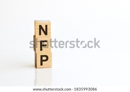 Three wooden cubes with letters NFP - Nonfarm payrolls - on white table, more in background, space for text in right down corner