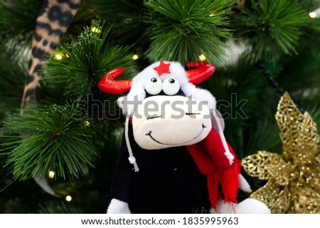 a toy bull in a white hat with a red star hangs on an evergreen tree