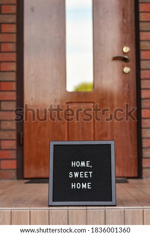 "Home sweet home" sign on black letterbox standing next to the house entrance door.