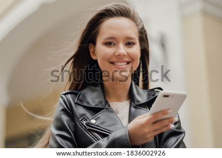 he holds a mobile phone in his hands, makes online purchases, smiles and shows his teeth. Brunette of Caucasian appearance, texting her friend