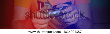 Male hands with game joystick, gamepad. The young guy is playing the console. Red blue neon light. Close up of man hands playing the video game at home.
