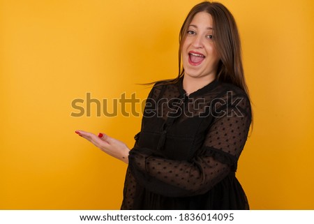 Positive glad female says: wow how exciting it is, has amazed expression, shows something on blank space with open hand over isolated gray background. Advertisement concept.