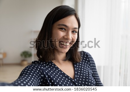 Close up of smiling young Vietnamese woman take self-portrait picture of herself in own house home. Happy millennial 20s asian female renter tenant make selfie on good quality smartphone camera.