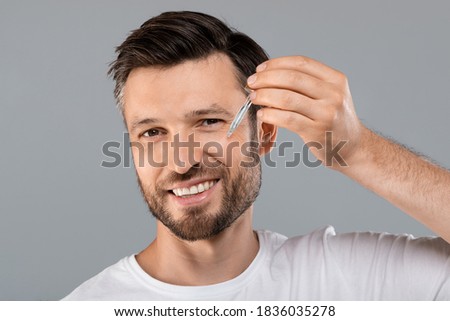 Middle-aged handsome man applying anti-aging serum and smiling at camera over gray studio background, empty space. Handsome cheerful man using nourishing serum for his face, closeup Royalty-Free Stock Photo #1836035278