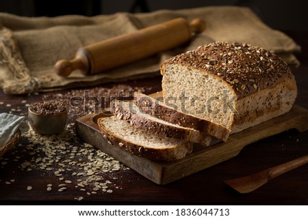 Rustic grain bread with oats, flax seeds, sunflower seeds and sesame seeds on a wooden board with a jute sack and a rolling pin on the background Royalty-Free Stock Photo #1836044713