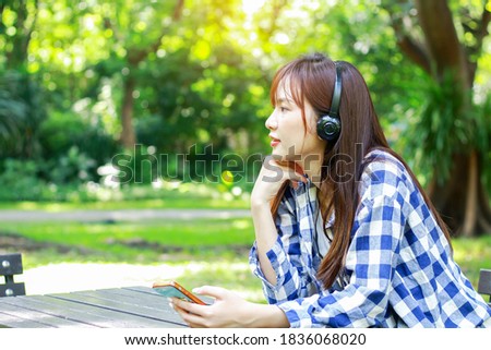 Asian women relax by listening to music on smartphones happily in the park. Concept of happy life of the new generation