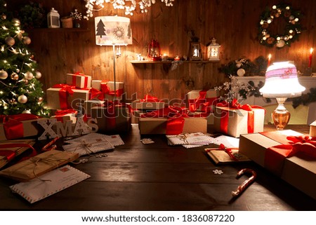 Santa Claus workshop home wooden decorated table with Merry Christmas tree, decor, wrapped gifts presents boxes on holiday eve in cozy home interior late in night with lamp light on xmas background. Royalty-Free Stock Photo #1836087220