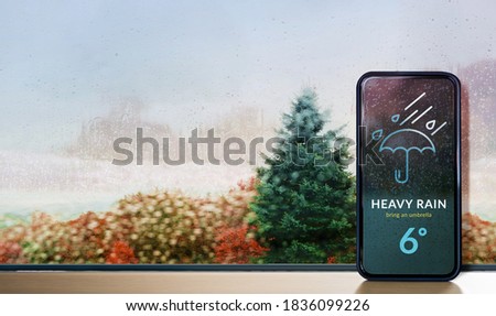 Rainy Day in Fall, Autumn and Winter Season Concept. Weather Information Forecast show on Mobile Phone Screen. View from Inside, through Glass Window Royalty-Free Stock Photo #1836099226