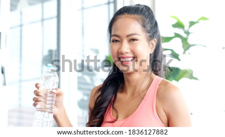 Young beautiful asian woman drinking water after exercise at home, Happy asia girl smiling while holding water bottle, people and healthy lifestyles