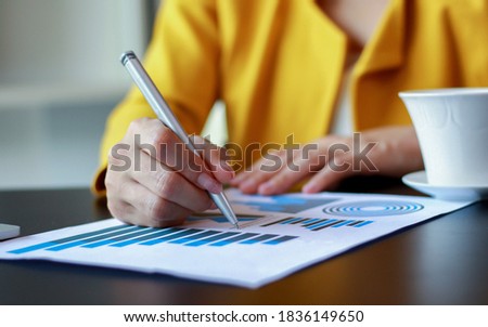  Hand of a business woman holds a pen and looks at graphs, tables, and market data