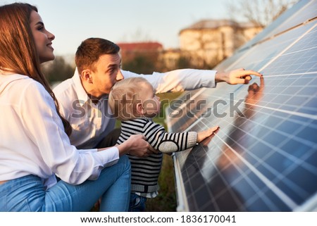 Side close-up shot of a young modern family with a little son getting acquainted with solar panel on a sunny day, green alternative energy concept Royalty-Free Stock Photo #1836170041