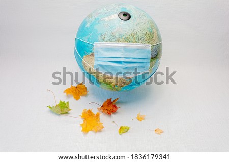 Globe wears a medical mask
  and maple leaves on a white background. Concept, our world is infected with coronavirus. Autumn, stay at home in quarantine