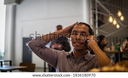 A portrait of young Asian Malay businessman sitting inside of cafe or restaurant and talking on the phone with clients and customers. Having serious conversation about work. Selective focus.