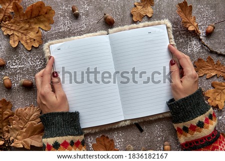 Autumn composition made of brown dried leaves and acorns on dark concrete background. Template mockup blank notebook and hand with a pen. Fall, halloween. Flat lay, copy space background