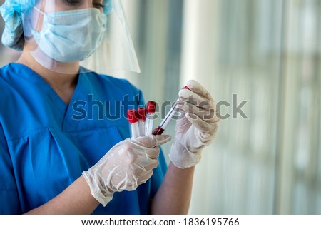 Woman doctor in blue uniform face mask face shield and white gloves hold test tube with positive result for covid 19. pandemic concept