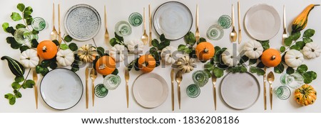 Fall table setting for celebration Thanksgiving or Friendsgiving day, family party or gathering. Flat-lay of plates, cutlery, glassware, colorful pumpkins and leaves over white background, top view
