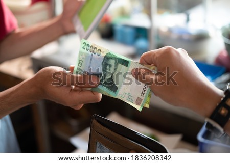 close up of the hand of an asian buyer paying in rupiah to a food stall seller after eating at a food stall Royalty-Free Stock Photo #1836208342
