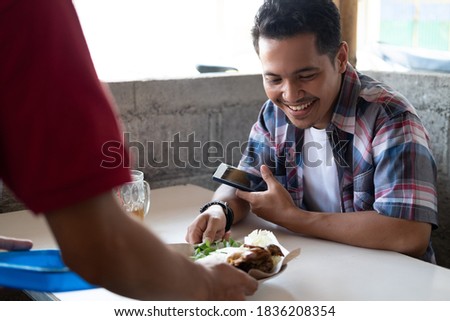 the buyer smiles holding his cellphone when the waiter at the food stall presents his order Royalty-Free Stock Photo #1836208354