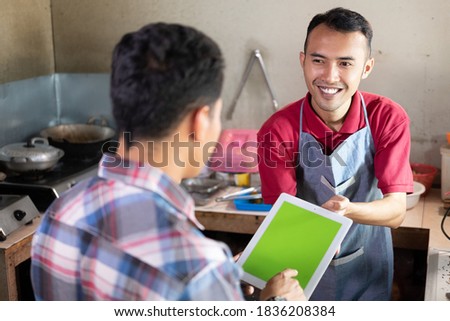 The male waiter smiled kindly while serving the customer holding a tablet pc at the food stall Royalty-Free Stock Photo #1836208384
