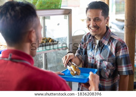 The seller holds the tray serving the buyer choosing side dishes with a food stall background Royalty-Free Stock Photo #1836208396