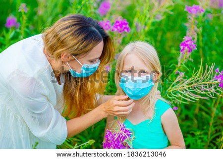 Mom adjusts the medical mask on her daughter while walking on the street in the park