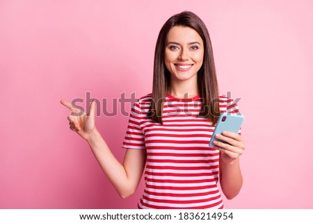 Photo portrait of girl keeping cellphone pointing at blank space isolated on pastel pink color background