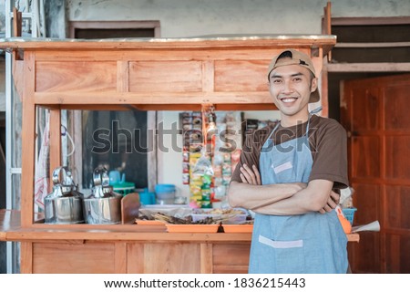 angkringan seller in apron smiles with crossed hands while standing in front of the cart stall Royalty-Free Stock Photo #1836215443