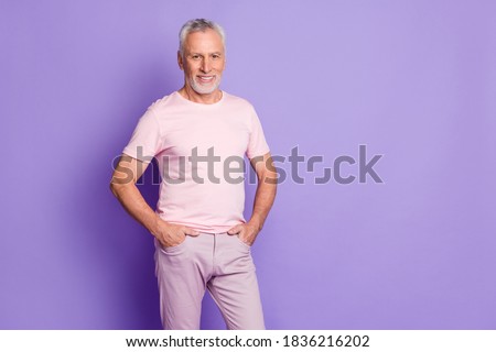 Photo of cool old man hands pockets beaming smile look camera wear pink t-shirt pants isolated violet color background