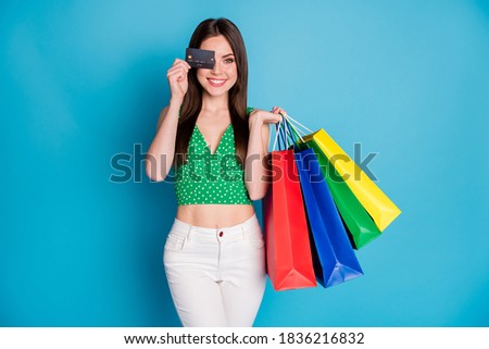 Photo of positive cheerful girl close cover eye credit card enjoy shopping hold many bags wear white pants trousers green dotted tank-top isolated over blue color background