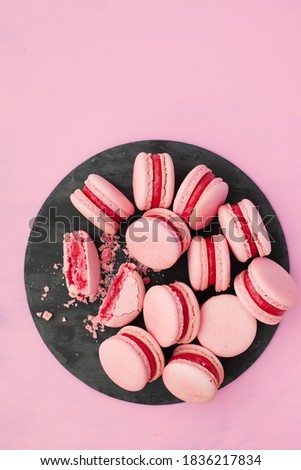 Colorful macarons cakes. Small sweet raspberry pink French macaroons on a plate with heart over pink backround, sweet background. Flat lay, top view, copy space