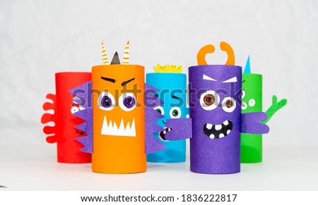 Halloween decoration. DIY and kids creativity concept. Monsters from toilet rolls and colored paper on a white table.