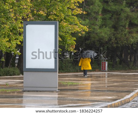 Man in yellow raincoat walking on a rainy day and billboard 