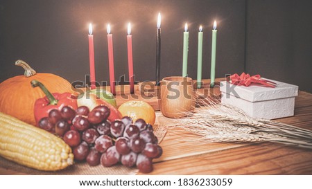 Kwanzaa holiday concept with decorate seven candles red, black and green, gift box, pumpkin,corn and fruit on wooden desk and black background.vintage effect