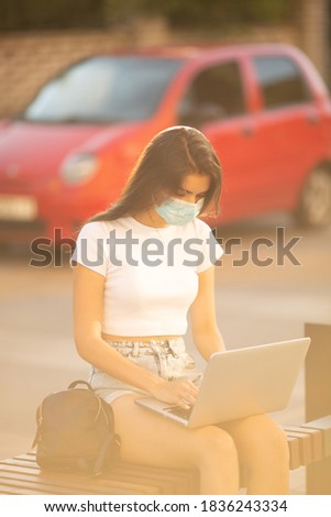 Young female. freelance woman in white t shirt wearing mask working on laptop pc computer,  in city public place,  sunshine lawn outdoors, Lifestyle concept with copy space.