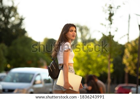 Young female. freelance woman in white t shirt wearing mask holding  laptop pc computer,  in city public place,  sunshine lawn outdoors, Lifestyle concept with copy space.