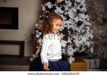 Very nice charming little girl  sitting on a child's bed and laughs loudly on the background of Christmas trees in dark interior of the house.