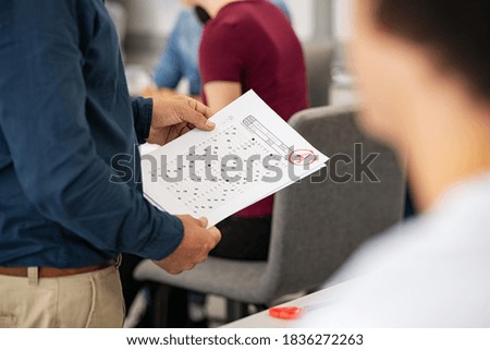 Close up of teacher hands holding test result in high school class. University professor holding answer sheets with grades while distributing them to the college students. Lecturer giving test results Royalty-Free Stock Photo #1836272263