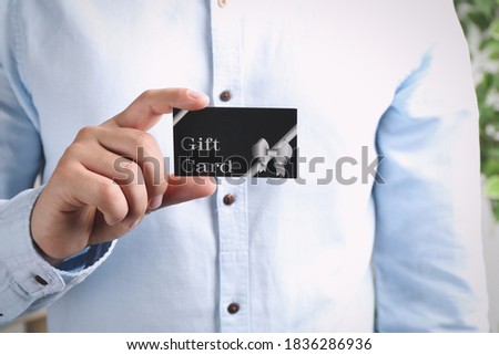 Man with gift card on blurred background, closeup