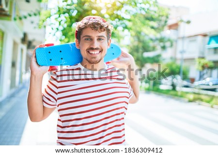 Young caucasian skater man smiling happy holding skate walking at street of city.