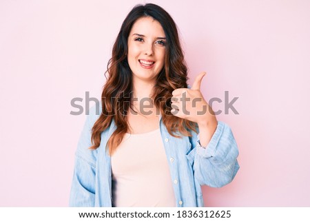 Young beautiful brunette woman wearing casual clothes over pink background smiling happy and positive, thumb up doing excellent and approval sign 