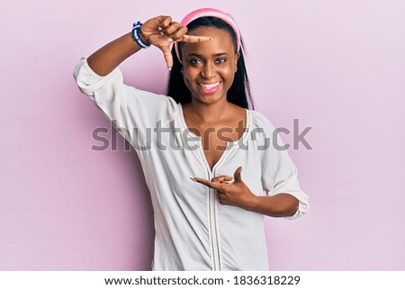 Young african woman wearing casual clothes over pink background smiling making frame with hands and fingers with happy face. creativity and photography concept. 