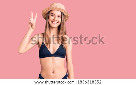 Young beautiful girl wearing bikini and hat showing and pointing up with fingers number two while smiling confident and happy. 