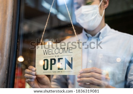 Cafe or restaurant and business reopen after Coronavirus quarantine is over. Man with face mask turning a sign from closed to open on a door shop. Small food shop business after post covid lockdown.